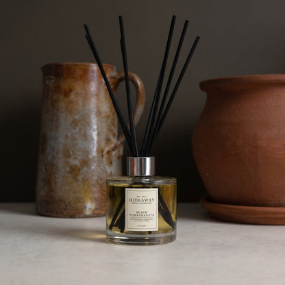 Mood-lit living room setup featuring a Hideaway Home Fragrances black pomegranate reed diffuser next to fresh flowers
