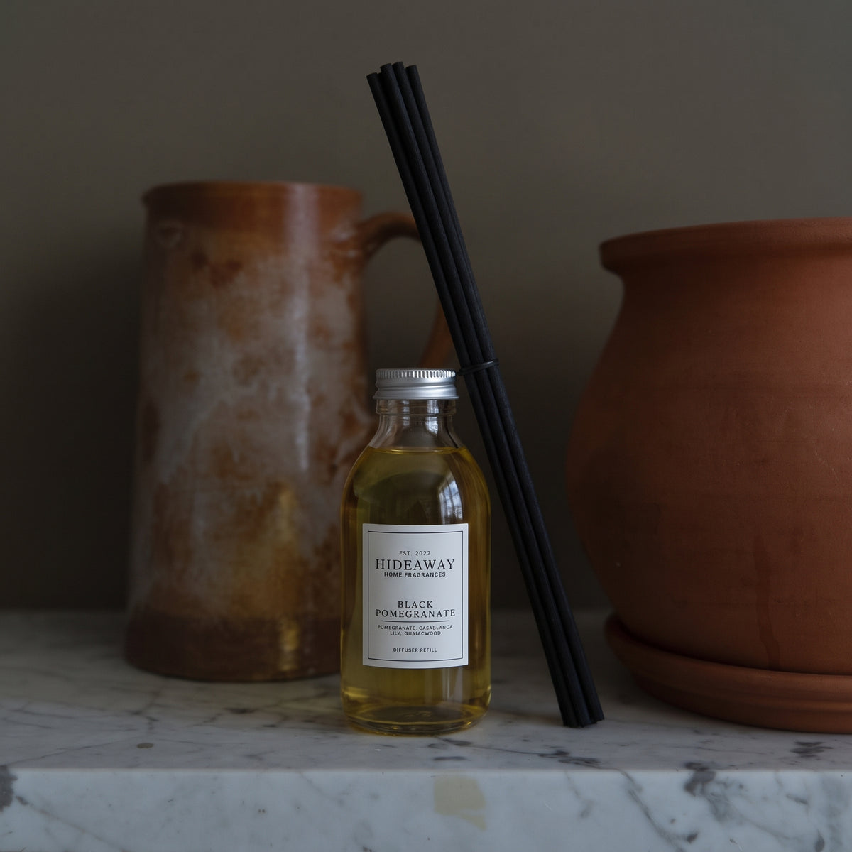 Hideaway Home Fragrances black pomegranate reed diffuser styled on a marble tray on a sunlit living room table