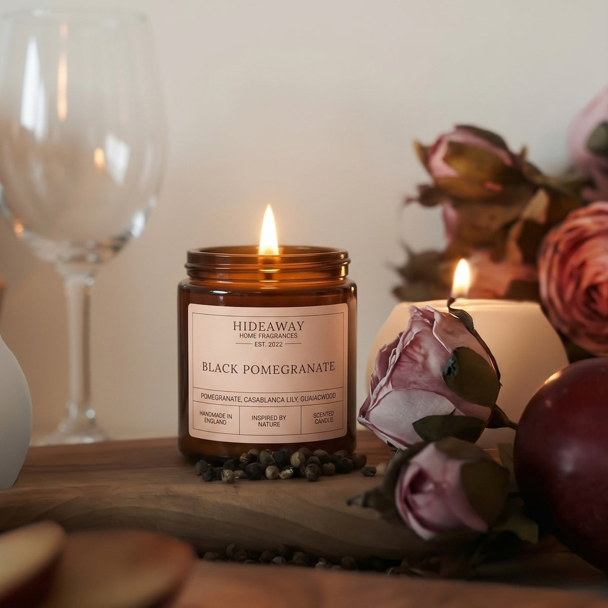 Lit black pomegranate amber glass candle casting a warm cosy glow on a wooden table, crafted by Hideaway Home Fragrances