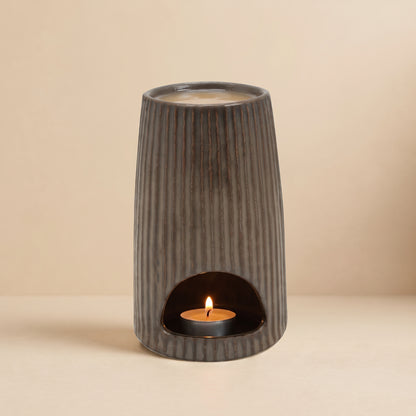 The glowing Bronze Ribbed Ceramic Wax Melt Burner by Hideaway Home Fragrances in a dark room, with a lit tealight inside and melting wax on top, diffusing cozy home fragrance.