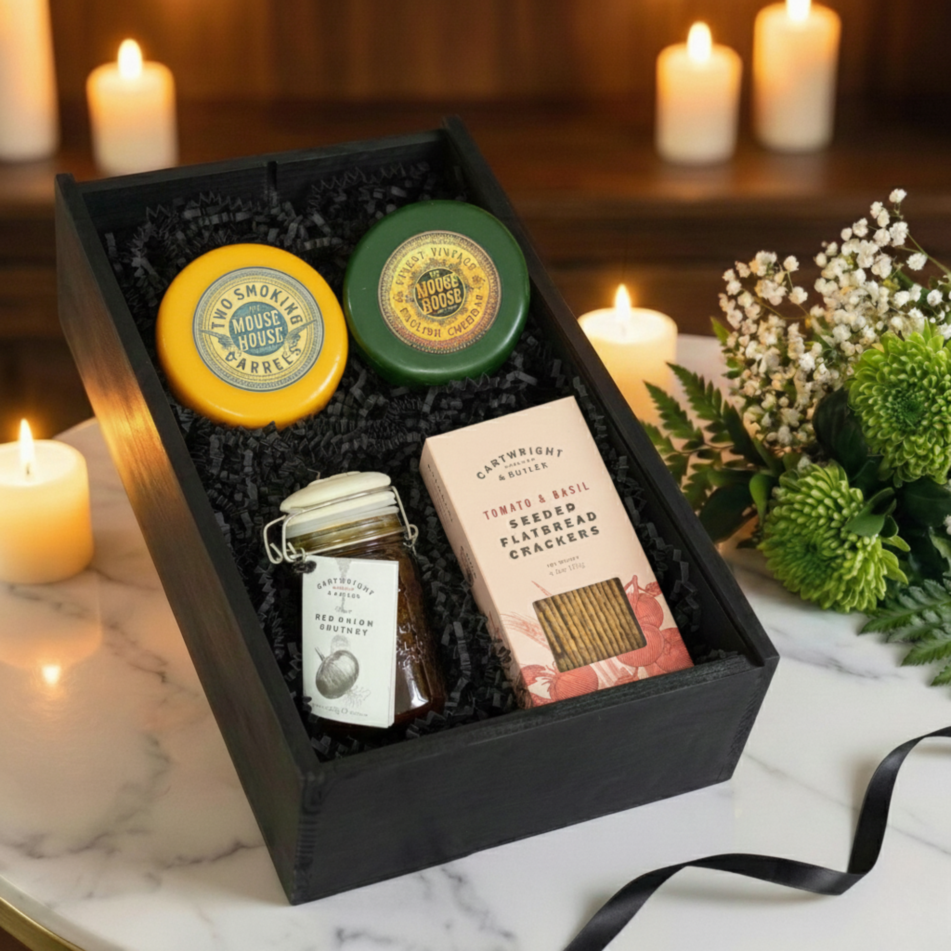 Close up of wax-coated cheese truckle and jar of artisan chutney next to a black presentation box.