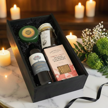 Close up of red wine bottle next to a wax-coated cheese truckle and open jar of chutney.