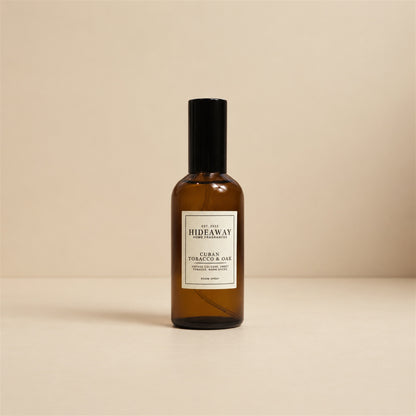 Hideaway Home Fragrances cuban tobacco and oak room spray styled on a wooden shelf next to leather-bound books.