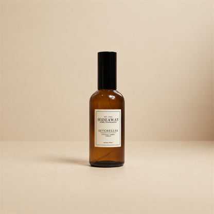 Hideaway Home Fragrances seychelles room spray styled on a sunlit bedside table beside woven textured decor and fresh jasmine flowers.