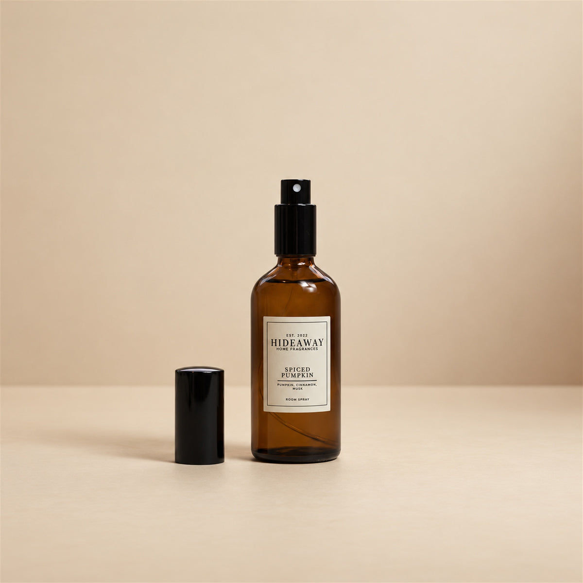 Hideaway Home Fragrances spiced pumpkin room spray styled on a wooden mantlepiece beside decorative mini pumpkins and cinnamon sticks.