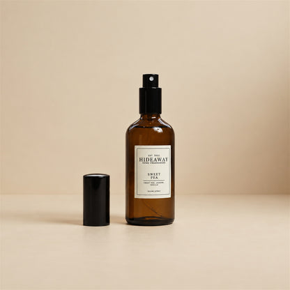 Fine mist spraying from the Hideaway Home Fragrances sweet pea room spray bottle to diffuse soft rose, jasmine, and creamy vanilla notes into the room.