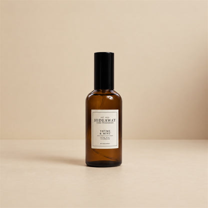 Hideaway Home Fragrances thyme and mint room spray styled on an oak shelf next to fresh potted spearmint and cut herbs.