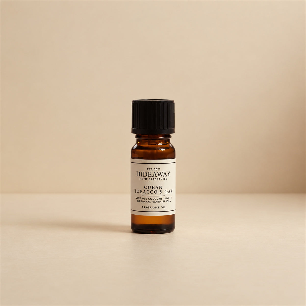 Dropper dispensing drops of Hideaway Home Fragrances cuban tobacco and oak fragrance oil into an electric aroma diffuser on a dark wood table.