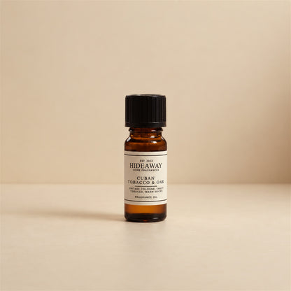 Dropper dispensing drops of Hideaway Home Fragrances cuban tobacco and oak fragrance oil into an electric aroma diffuser on a dark wood table.