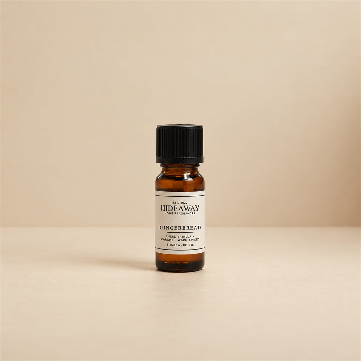 Glass dropper dispensing Hideaway Home Fragrances gingerbread fragrance oil into a ceramic wax burner beside cinnamon sticks and golden caramel.