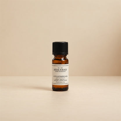 Glass dropper dispensing Hideaway Home Fragrances gingerbread fragrance oil into a ceramic wax burner beside cinnamon sticks and golden caramel.
