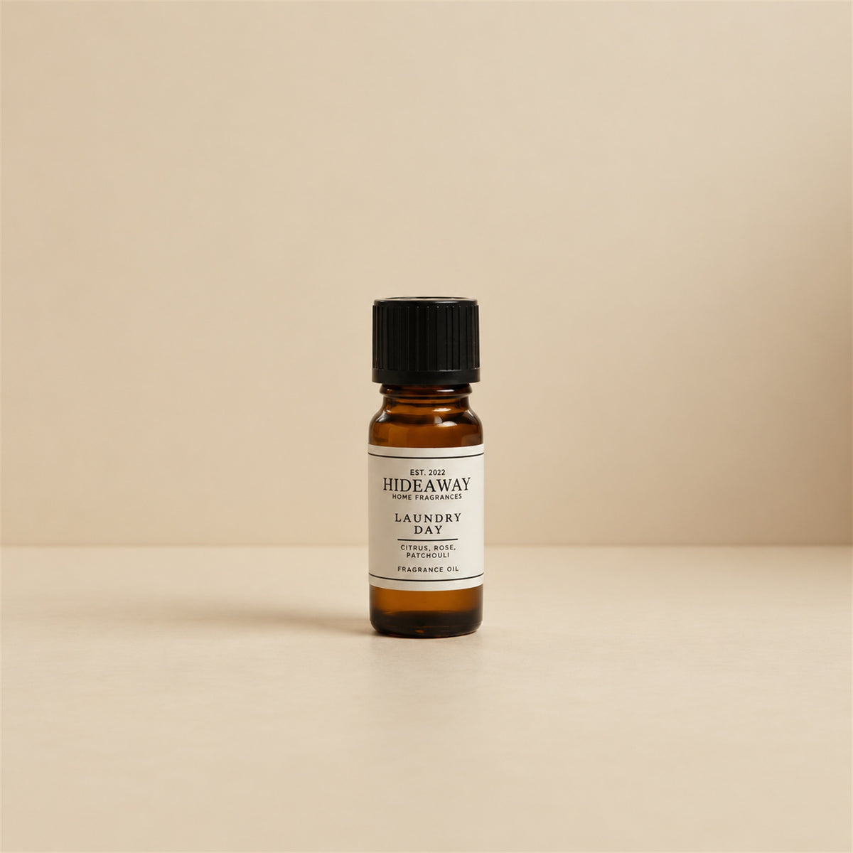 Glass dropper dispensing Hideaway Home Fragrances laundry day fragrance oil into an aroma diffuser beside folded white linen towels.