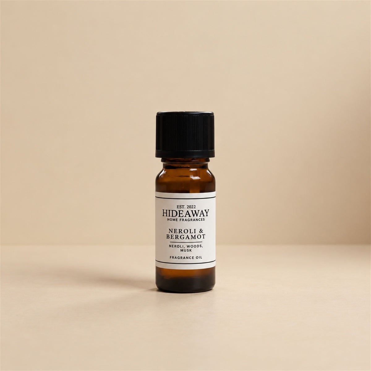Glass dropper dispensing Hideaway Home Fragrances neroli and bergamot fragrance oil into an electric aroma diffuser beside delicate white floral blossoms.