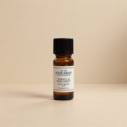 Glass dropper dispensing Hideaway Home Fragrances neroli and bergamot fragrance oil into an electric aroma diffuser beside delicate white floral blossoms.