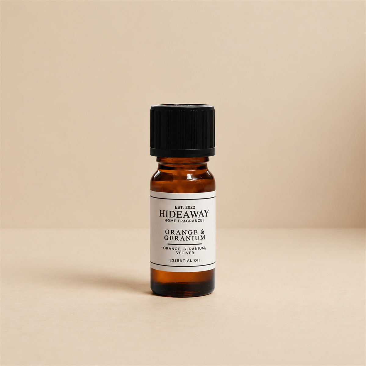 Glass dropper dispensing Hideaway Home Fragrances orange and geranium fragrance oil into a ceramic wax burner beside fresh orange peel and botanical leaves.