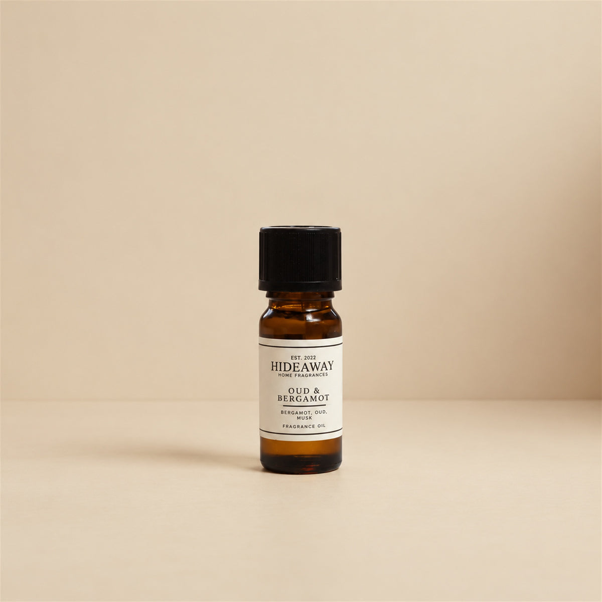 Glass dropper dispensing Hideaway Home Fragrances oud and bergamot fragrance oil into a ceramic burner beside cedarwood accents and warm spices.
