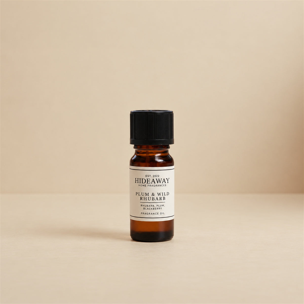 Glass dropper dispensing Hideaway Home Fragrances plum and wild rhubarb fragrance oil into a ceramic aroma burner beside fresh orchard fruit.