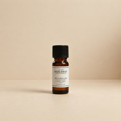 Glass dropper dispensing Hideaway Home Fragrances seychelles fragrance oil into an electronic diffuser beside white jasmine petals and coastal decor.