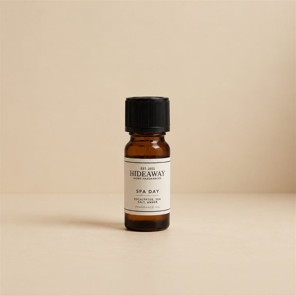 Glass dropper dispensing Hideaway Home Fragrances spa day fragrance oil into an aroma diffuser beside fresh eucalyptus sprigs and white rolled towels.