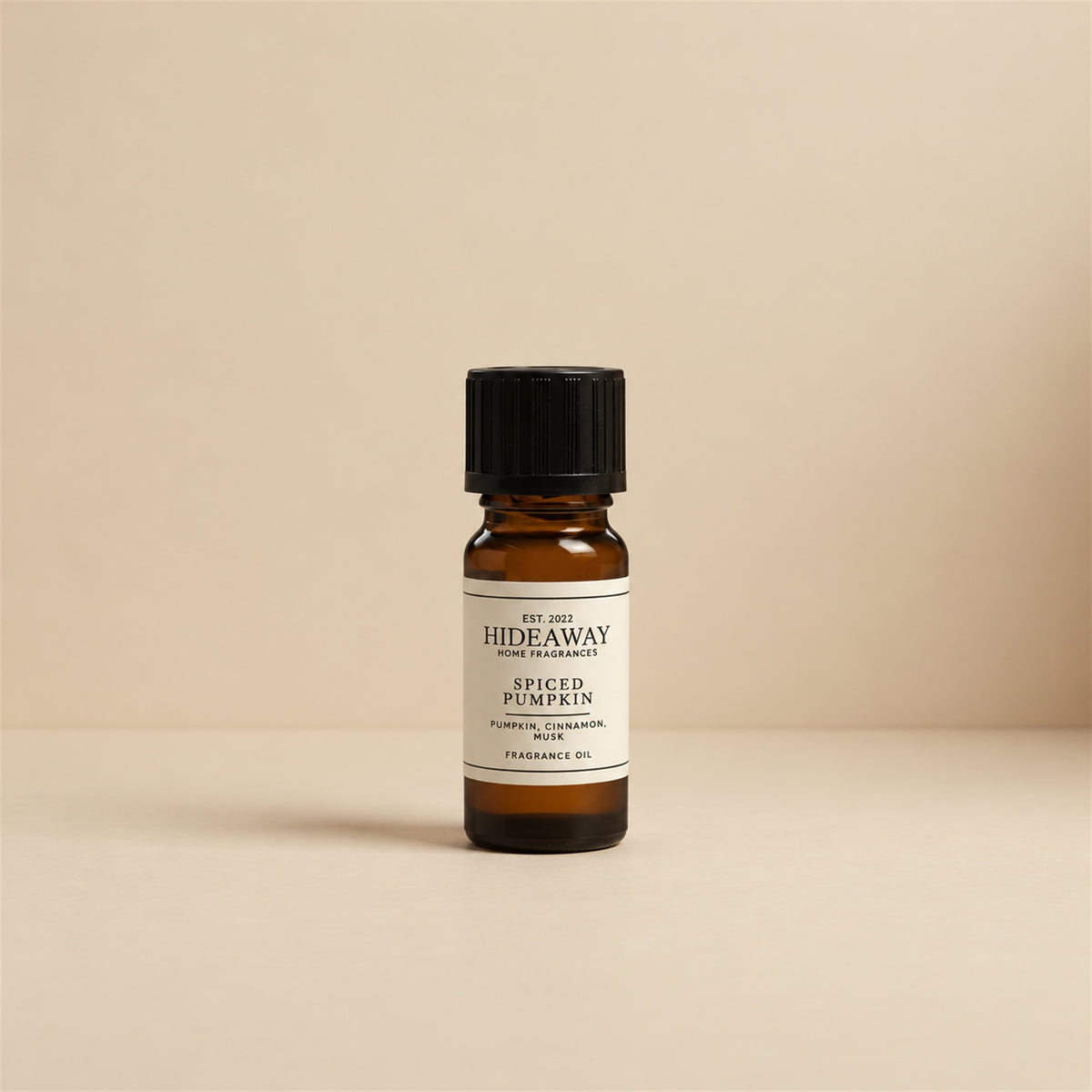 Glass dropper dispensing Hideaway Home Fragrances spiced pumpkin fragrance oil into a ceramic wax burner beside cinnamon sticks and decorative mini pumpkins.