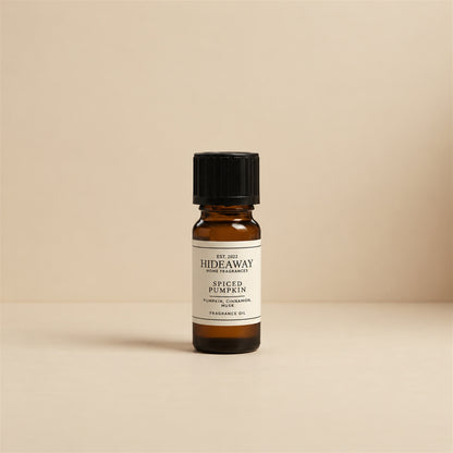 Glass dropper dispensing Hideaway Home Fragrances spiced pumpkin fragrance oil into a ceramic wax burner beside cinnamon sticks and decorative mini pumpkins.