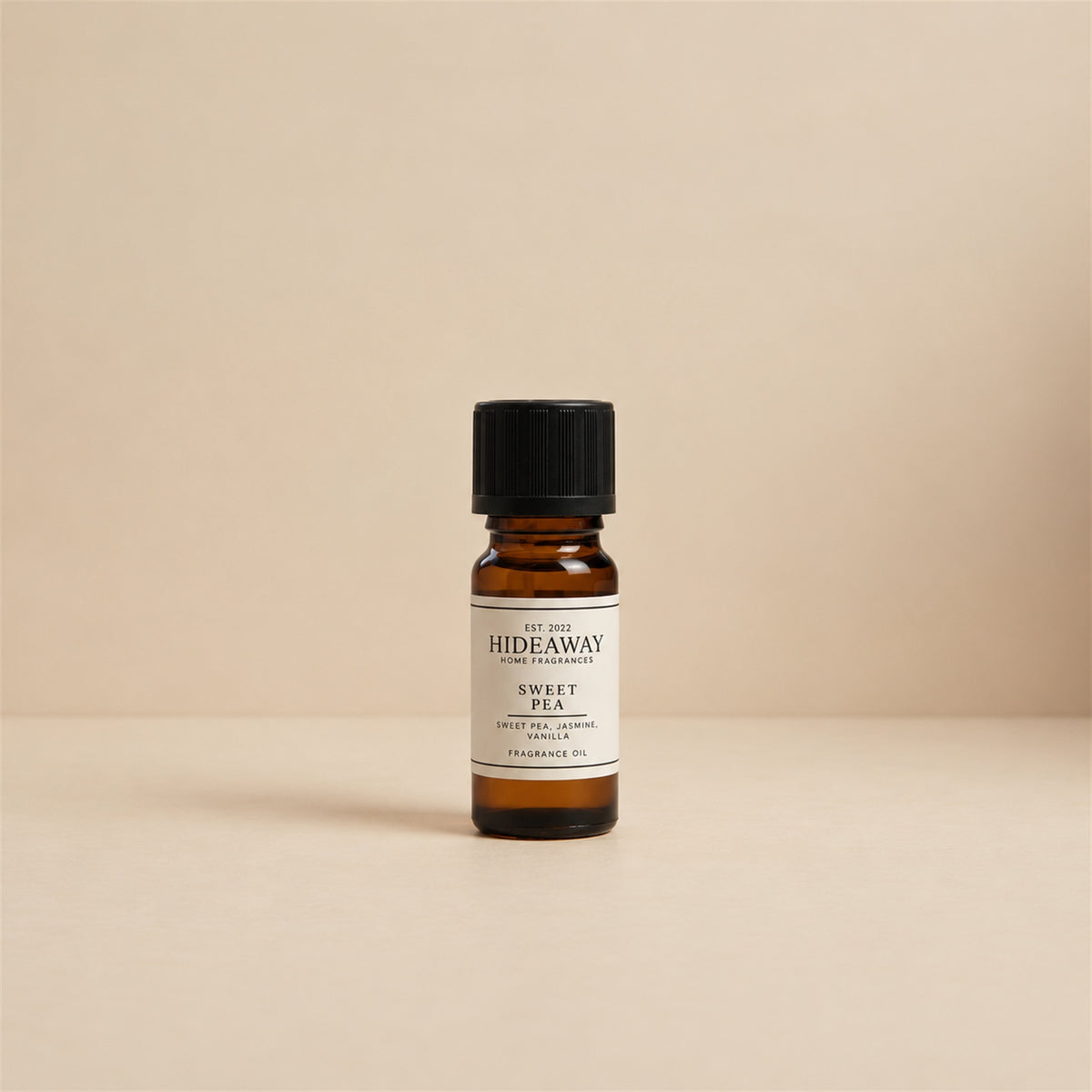 Glass dropper dispensing Hideaway Home Fragrances sweet pea fragrance oil into an aroma diffuser beside fresh pastel florals and green stems.