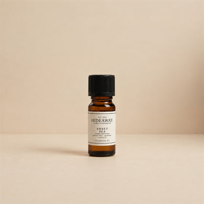 Glass dropper dispensing Hideaway Home Fragrances sweet pea fragrance oil into an aroma diffuser beside fresh pastel florals and green stems.