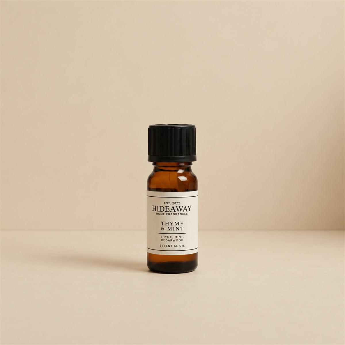 Glass dropper dispensing Hideaway Home Fragrances thyme and mint fragrance oil into a ceramic burner beside fresh herbal thyme and mint sprigs.