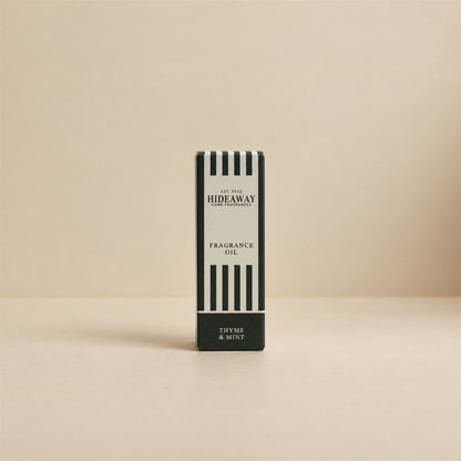 Packaged Hideaway Home Fragrances thyme and mint fragrance oil bottle standing beside its luxury retail box highlighting zesty bergamot, marjoram, and cedarwood notes.