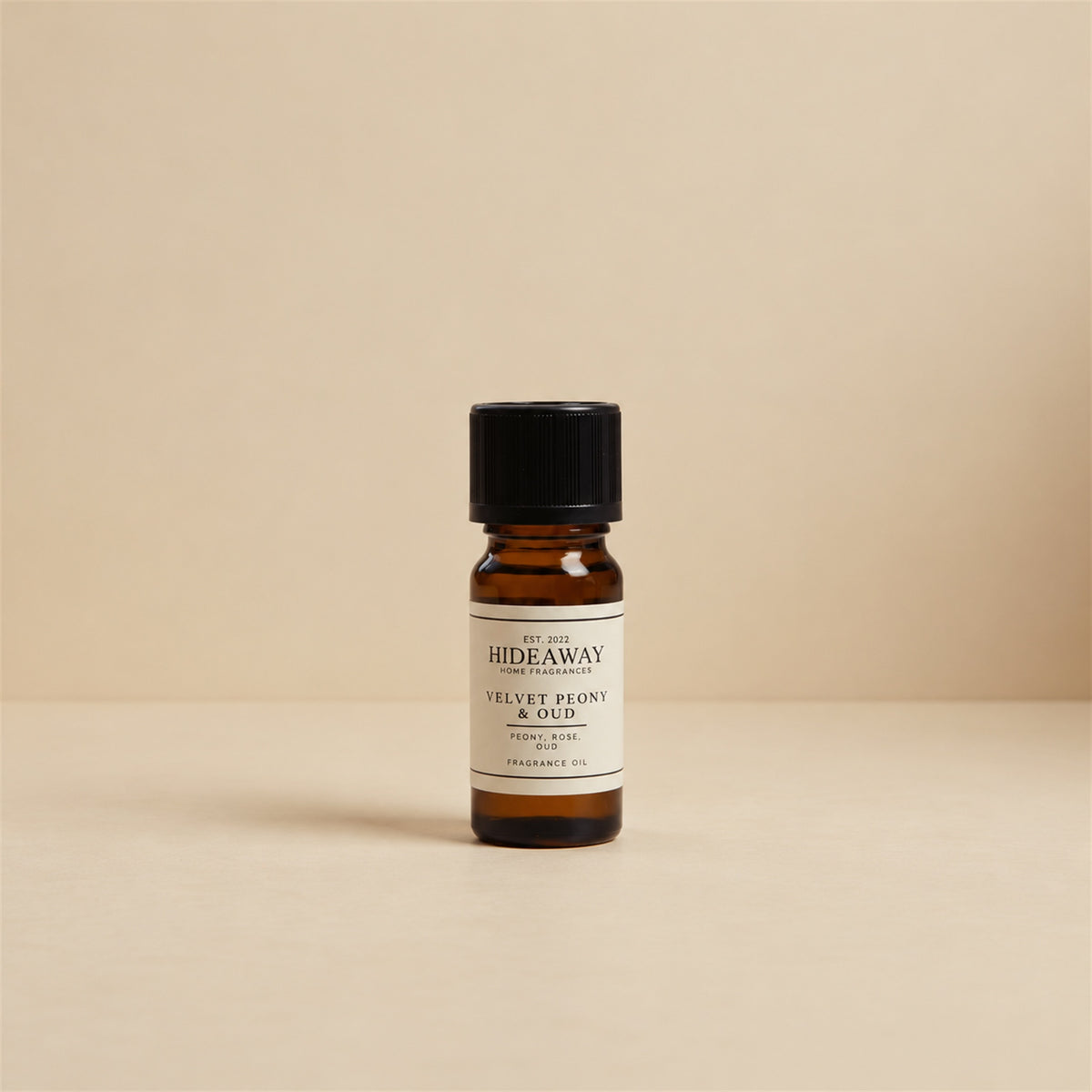 Glass dropper dispensing Hideaway Home Fragrances velvet peony and oud fragrance oil into a ceramic wax burner beside fresh deep pink peony petals.