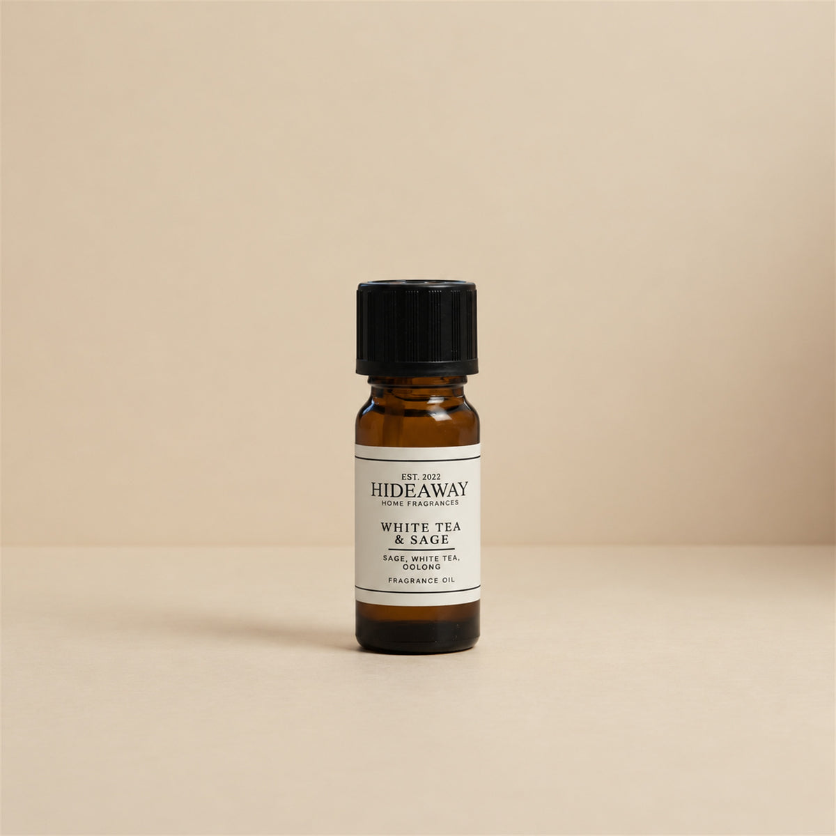 Glass dropper dispensing Hideaway Home Fragrances white tea and sage fragrance oil into a ceramic burner beside fresh herbal sage and mint leaves.