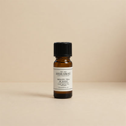 Glass dropper dispensing Hideaway Home Fragrances white tea and sage fragrance oil into a ceramic burner beside fresh herbal sage and mint leaves.
