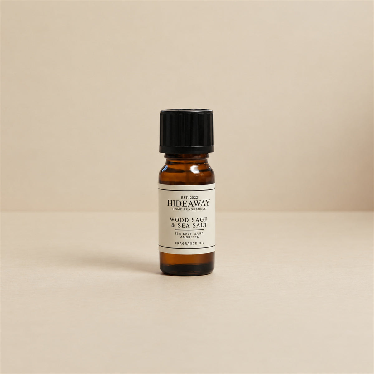 Glass dropper dispensing Hideaway Home Fragrances wood sage and sea salt fragrance oil into an aroma diffuser beside fresh sage leaves and natural sea stones.