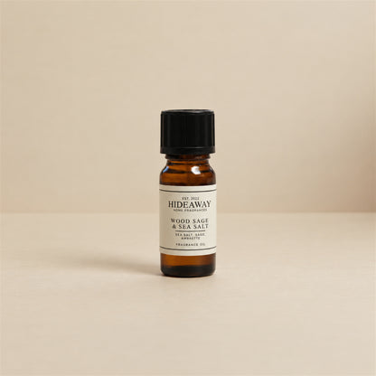 Glass dropper dispensing Hideaway Home Fragrances wood sage and sea salt fragrance oil into an aroma diffuser beside fresh sage leaves and natural sea stones.