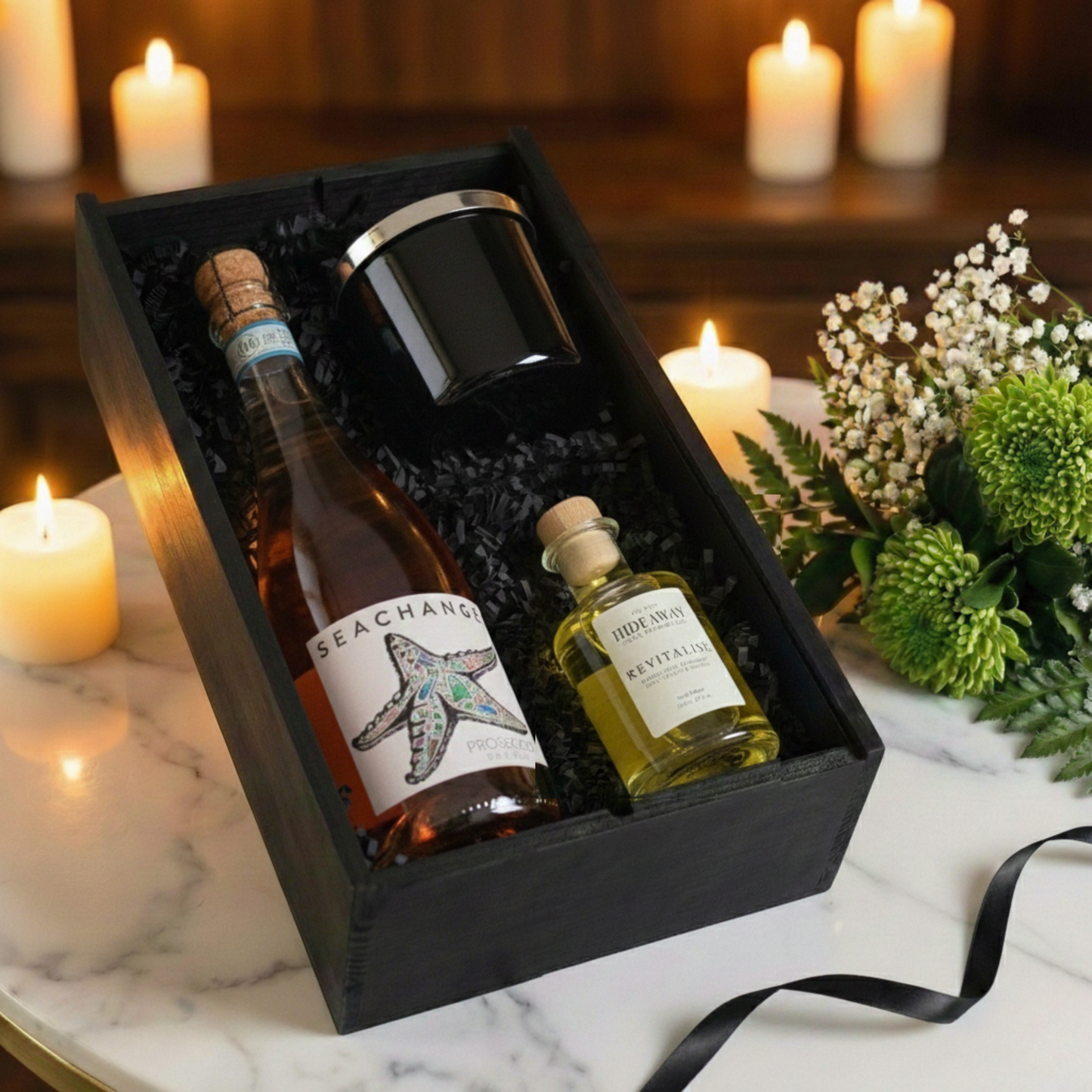 Close up of luxury home fragrance set with glass candle and reed diffuser next to a bottle of eco-friendly sparkling 