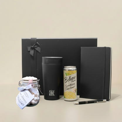 Close up of A5 cream paper notebook and rubberised ball pen next to a premium insulated coffee cup.