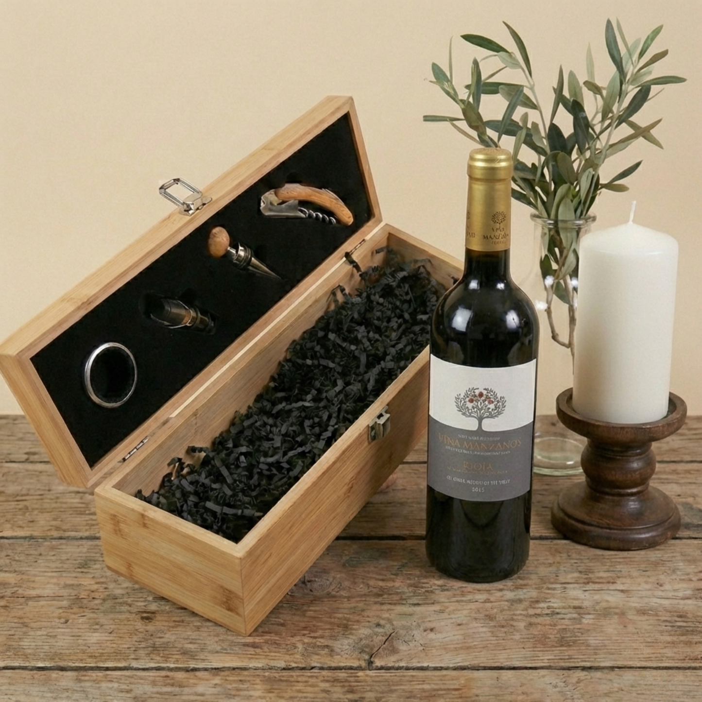 Open bamboo wine gift box displaying stainless steel pouring spout, wine ring, and corkscrew next to a bottle of Spanish red wine.