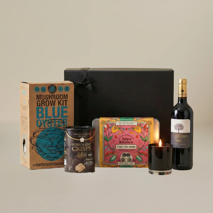 Cosy night in gift set flatlay with gourmet mushroom grow kit, luxury candle, Yorkshire crisps, and Spanish wine bottles.