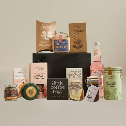 Luxury food hamper flatlay with wax coated cheese, jar of chutney, roasted peanuts, artisan chocolate, and tea temples.