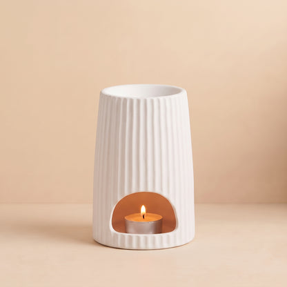 Warm glowing White Ribbed Ceramic Wax Melt Burner with lit tealight and melting wax tarts by Hideaway Home Fragrances