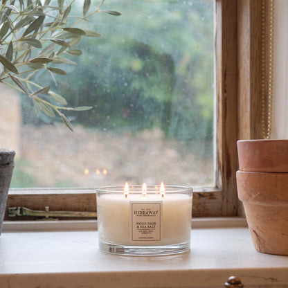 Hideaway Home Fragrances Wood Sage and Sea Salt 3 wick candle burning on a sunlit coffee table in a modern living room for a crisp coastal atmosphere